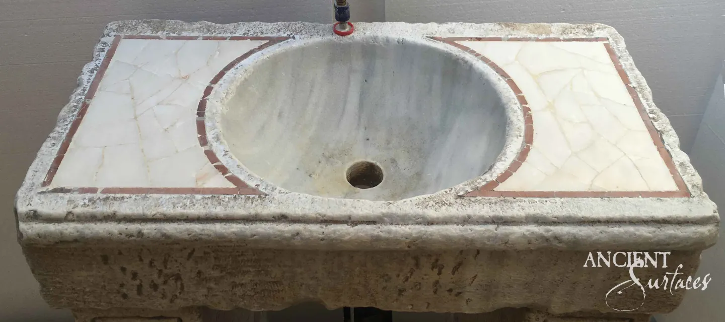 Reclaimed limestone sink slab with an oval carved basin, round drain and pale marble inlay panels bordered in terracotta banding