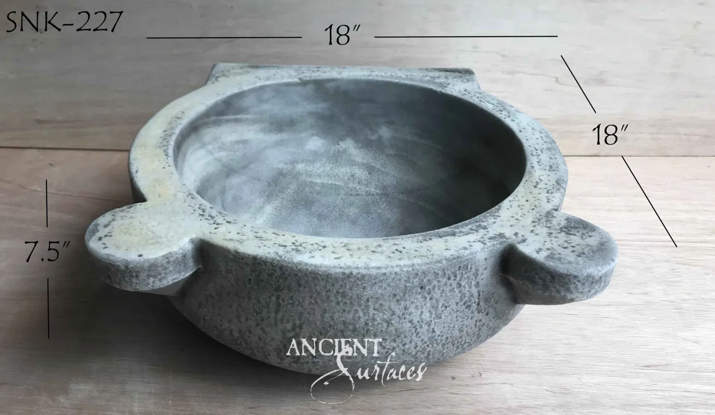 Small round reclaimed stone vessel basin with four blunt lug handles at the rim and a shallow smooth bowl in mottled grey stone