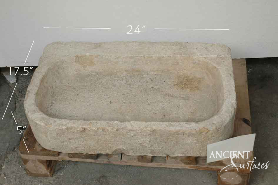 Shallow hand carved cream limestone basin with a rounded trough interior, visible chisel marks and a low broken rim