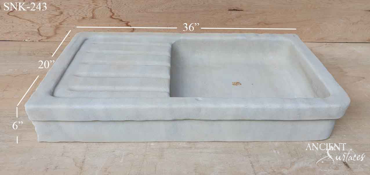 Wide pale reclaimed stone sink with a ribbed draining board on the left and an open rectangular basin on the right under a rounded rim