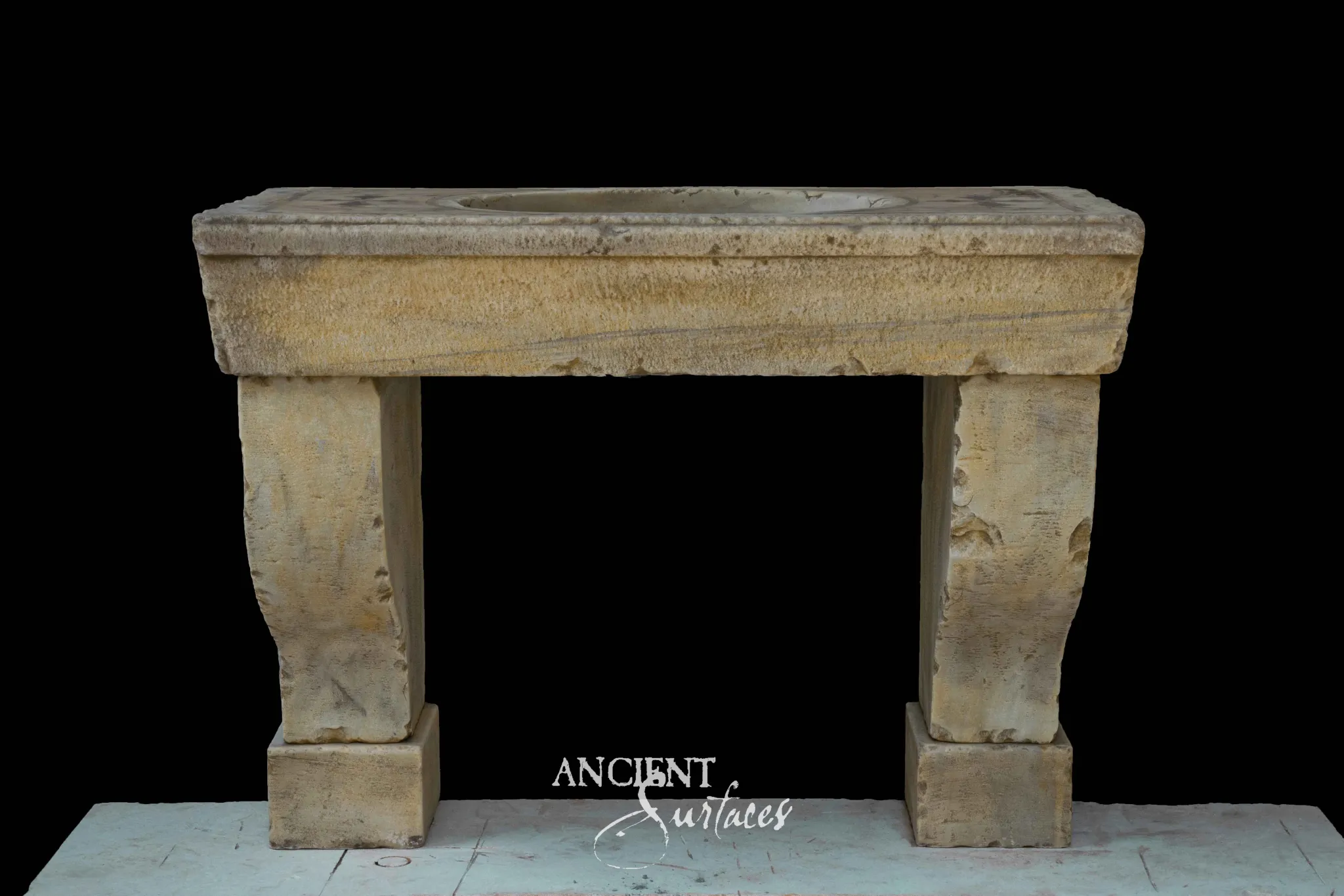 Honey toned reclaimed limestone console sink with a deep plain apron, thick slab top and two tapered legs on square plinths