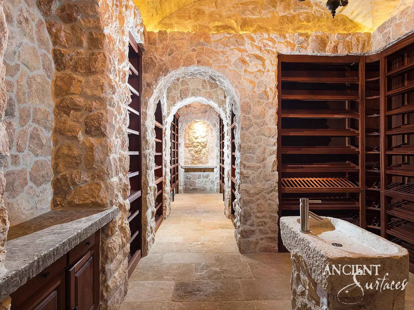 Long reclaimed limestone trough sink with a shallow hollowed basin and tall modern tap, built into a masonry pier in a vaulted stone cellar