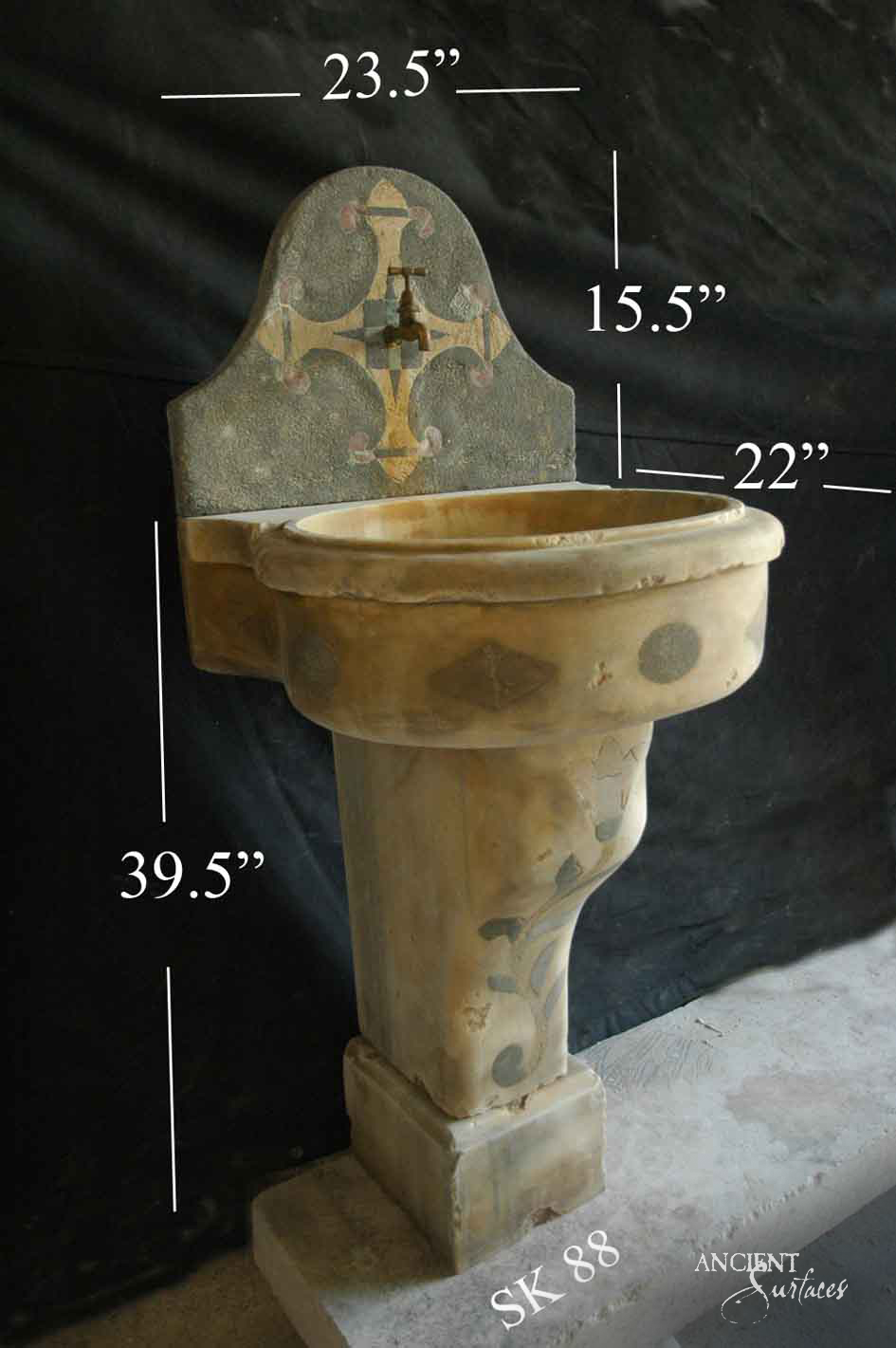 Honey toned limestone pedestal sink with a rolled rim bowl, dark lozenge inlays and an arched inlaid backsplash with a small spigot