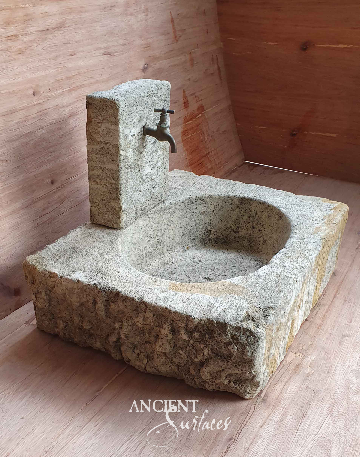 Compact reclaimed limestone sink with a deep round bowl and an integral upright stone block carrying a brass bibcock tap